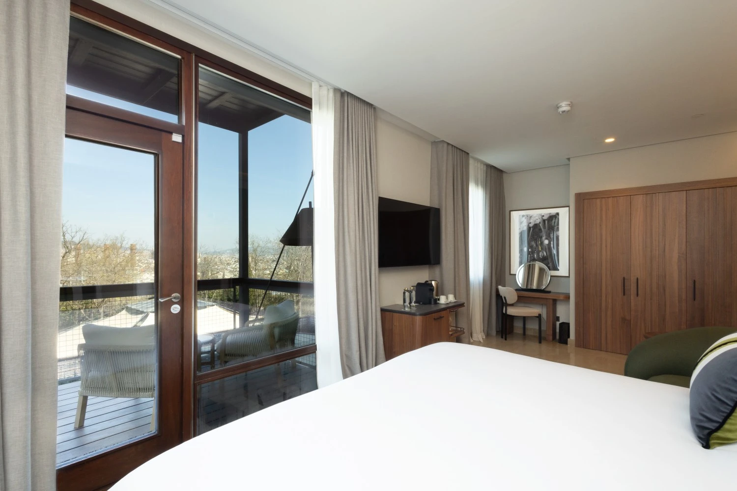 Vista desde la cama hacia los amplios ventanales, integrando el skyline de Barcelona en la atmósfera del dormitorio.