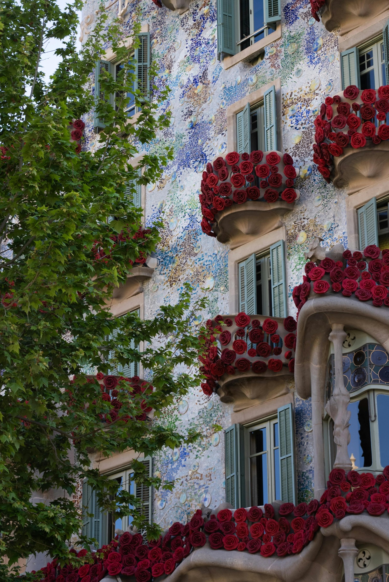 Vista exterior detallada de la Casa Batlló de Gaudí, con su fachada de mosaicos y múltiples balcones cubiertos por densos arreglos de rosas rojas por Sant Jordi